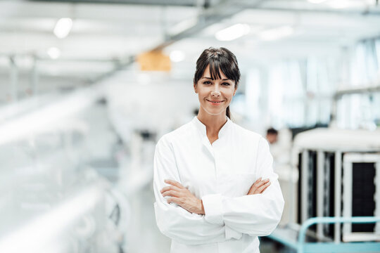 Smiling female scientist standing with arms crossed in bright laboratory