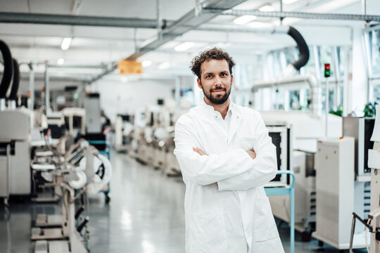 Male scientist wearing lab coat while standing with arms crossed at bright laboratory