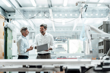 Smiling engineer discussing over laptop with male colleague in factory