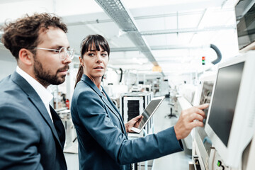 Confident businesswoman pointing at computer monitor while looking at businessman in industry