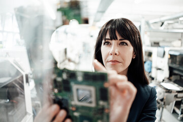 Confident female professional investigating while looking at circuit board in industry