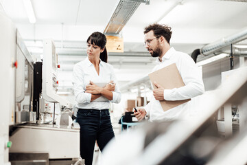 Male and female colleagues investigating machinery in manufacturing industry