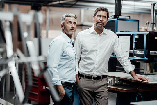 Male engineers in formals standing by workbench in factory