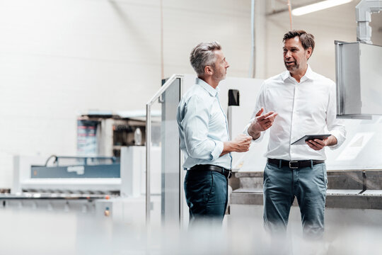 Smiling engineers discussing over digital tablet while standing in industry