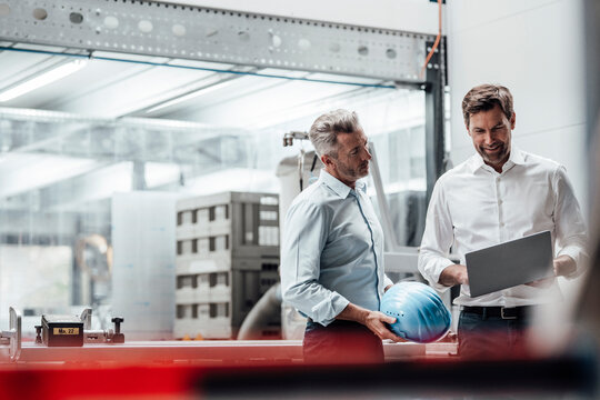 Smiling male engineer discussing with colleague over laptop in industry