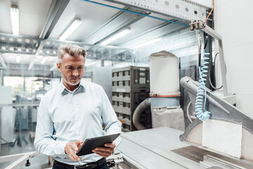 Mature businessman using digital tablet while standing by machinery in industry