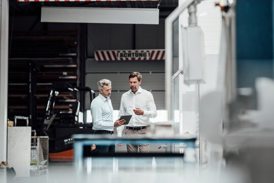 Businessmen discussing over digital tablet while standing in industry