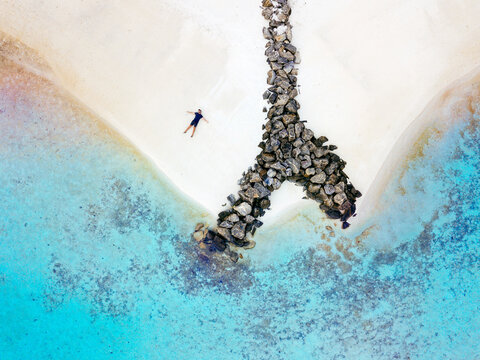 Maldives, Kaafu Atoll, Aerial view of man lying alone on sandy coastal beach of Huraa island