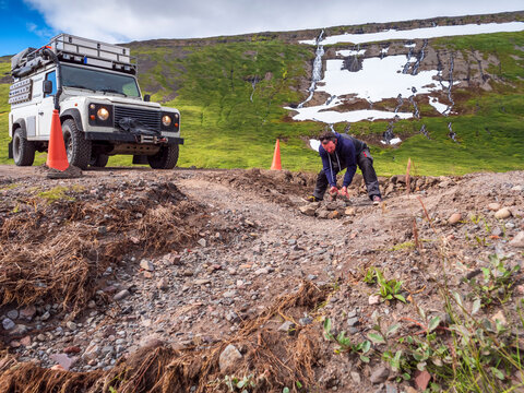 Man repairing pot hole in middle of dirt road leading to Drangajokull
