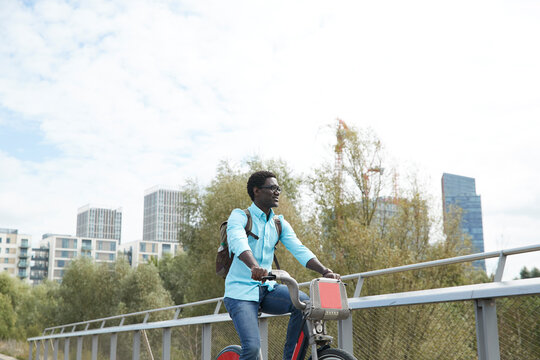 Mature man looking away while commuting on bicycle against sky in city