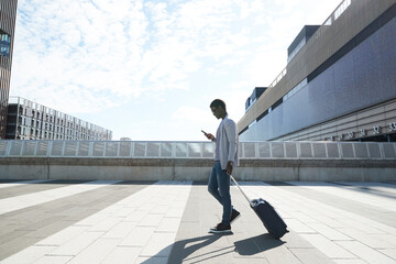 Businessman pulling luggage while using mobile phone against station in city