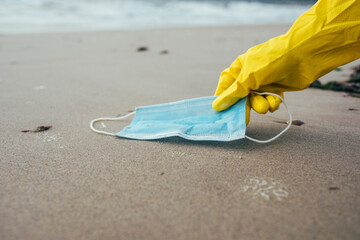 Female environmentalist picking up face mask while cleaning beach