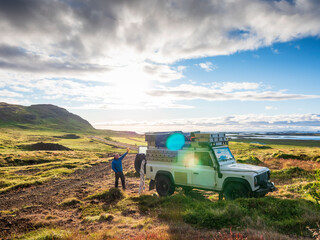 Sun setting over lone traveler standing behind off-road vehicle and waving at camera, Iceland