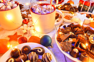 sweet food and decoration background for merry christmas or new year holiday with night illumination - chocolate candies, tangerines, cookies, marshmallow and cocoa latte on white wood