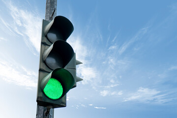 Traffic light in green color, with a blue sky and cloud in the background.