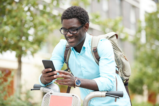 Smiling man text messaging on smart phone while leaning on bicycle