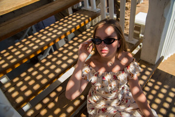A fashion portrait of a beautiful young female girl wearing sunglasses relaxing on a stairs on a sunny summer day in cafe on the beach. young slim beautiful woman summer vacation, sunny.