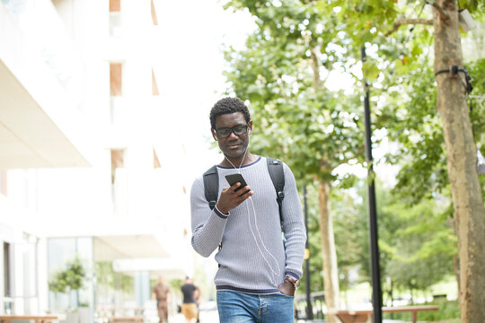 Mature male entrepreneur with hand in pocket listening music while walking against trees