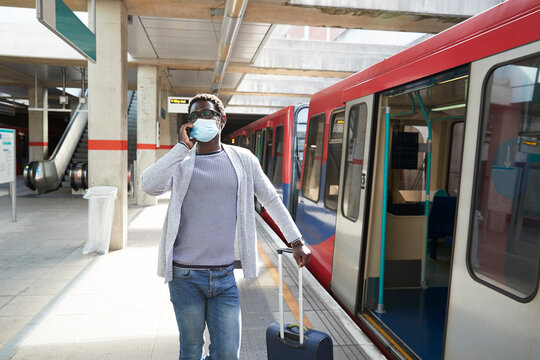 Mature businessman wearing protective face mask talking on phone at railroad station platform