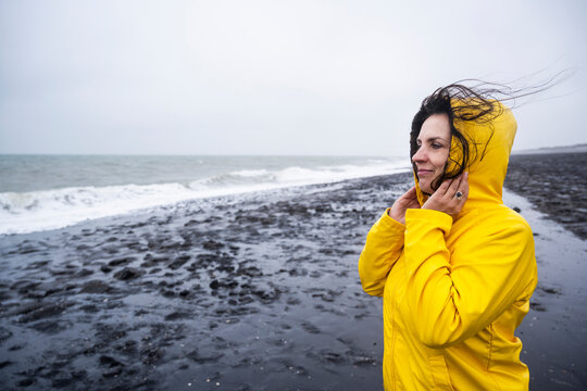 Smiling mature woman in yellow raincoat looking at view while standing on sea shore