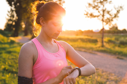 Young sportswoman examining time on smart watch standing in park