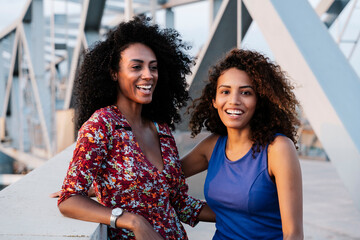 Happy young female friends by retaining wall on bridge