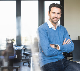Confident businessman sitting with arms crossed at office