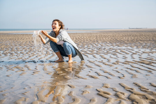 Cheerful young woman playing with water at seashore