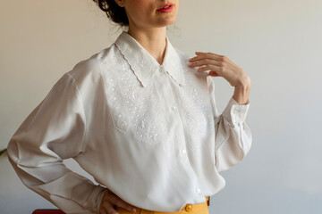 Woman wearing white shirt with hand on hip standing against wall