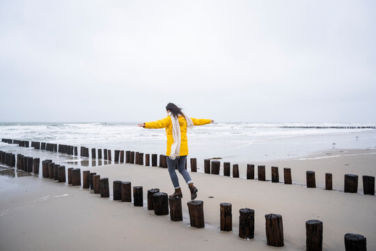 Woman walking on wooden posts at beach against sky
