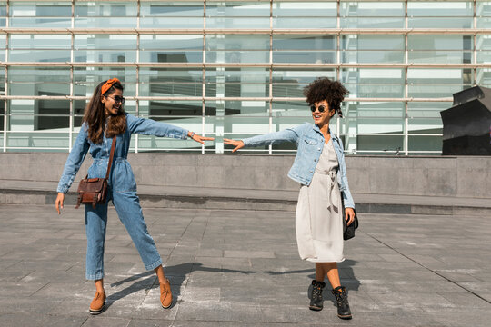 Smiling female friends stretching hand towards each other while standing on rooftop