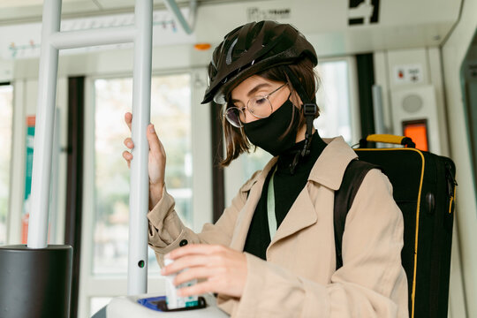Woman wearing face mask and cycling helmet putting validating ticket in machine while inside tram