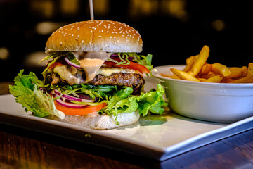 Delicious juicy burger with herbs and fries on the table. Cheese burger with beef, patty, tomato and onion.