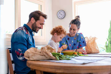 Happy woman looking at son holding green pea by father in kitchen