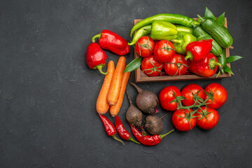 Vegetable basket with a bunch of green and peppers cucumber and tomatoes with stem carrots on dark background above view