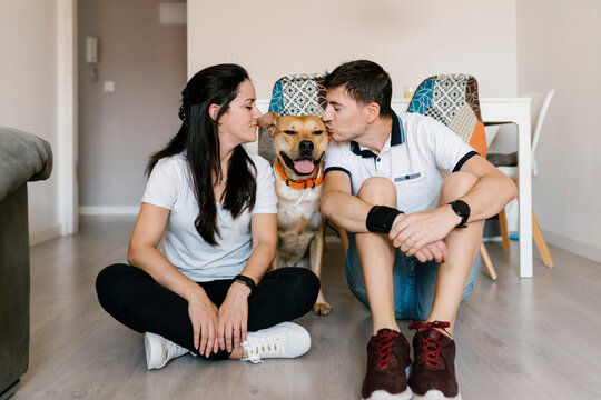 Couple kissing dog while sitting on floor at home
