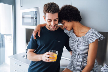 Loving interracial couple embracing happily while drinking juice