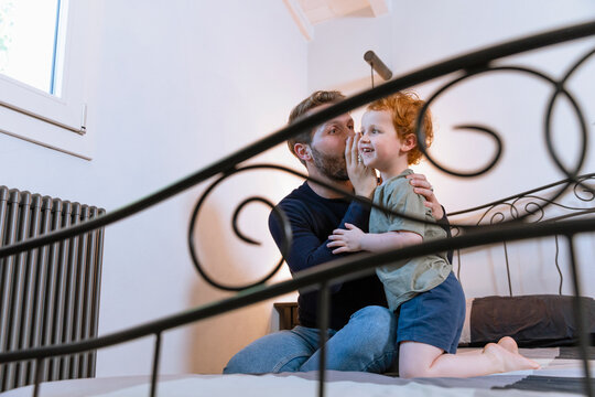 Father whispering to son on bed at home
