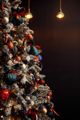 Photo of decorated christmas tree with colorful balls standing on dark wall with lamps background with copyspace