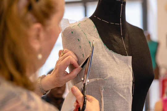 Close-up of senior designer cutting fabric on mannequin with scissors in atelier