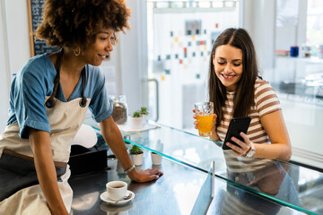 Beautiful female customer showing smart phone to owner in coffee shop
