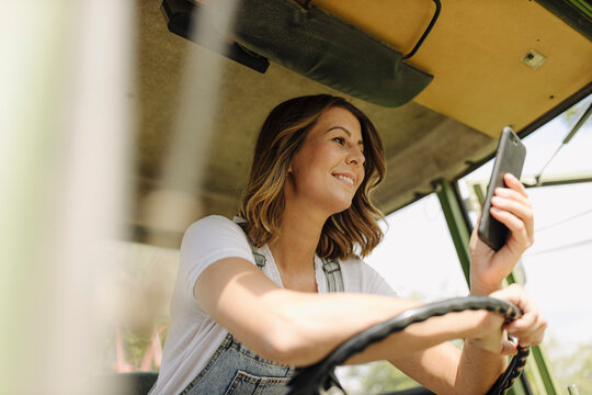 Smiling young woman using mobile phone in a tractor