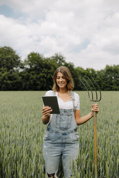 Young woman with hay fork and tablet standing in a grain field in the countryside