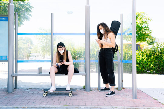 Two women with protective face masks waiting at bus station