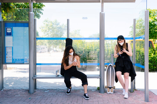 Two women with protective face masks waiting at bus station