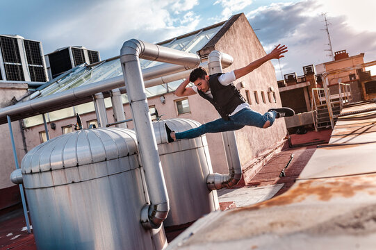 Stylish bboy performing a break dance jump between metallic pipes in the rooftop of a building 