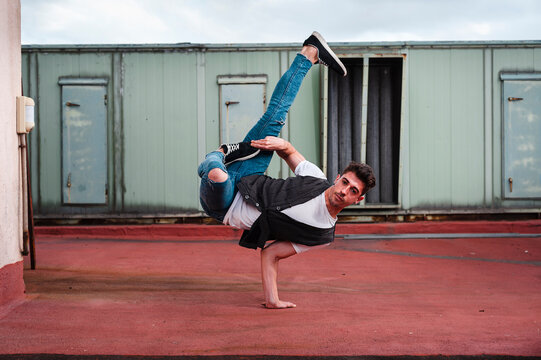 Stylish bboy performing a break dance stance close to green machinery in the rooftop of a building 