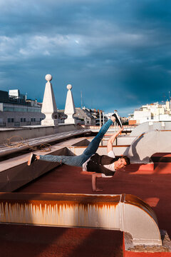 Stylish bboy performing a break dance stance metallic pipes in the rooftop of a building at sunset