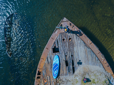Russia, Murmansk Oblast, Kolsky District, Teriberka, Sup surfer on shipwreck on Barents Sea, aerial view