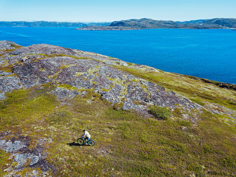 Russia, Murmansk region, Kolsky District, Teriberka, Man cycling on coastline, aerial view